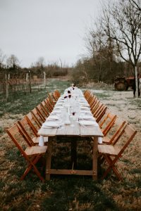 Long wooden table with chairs in a rustic outdoor setting, perfect for weddings or events.