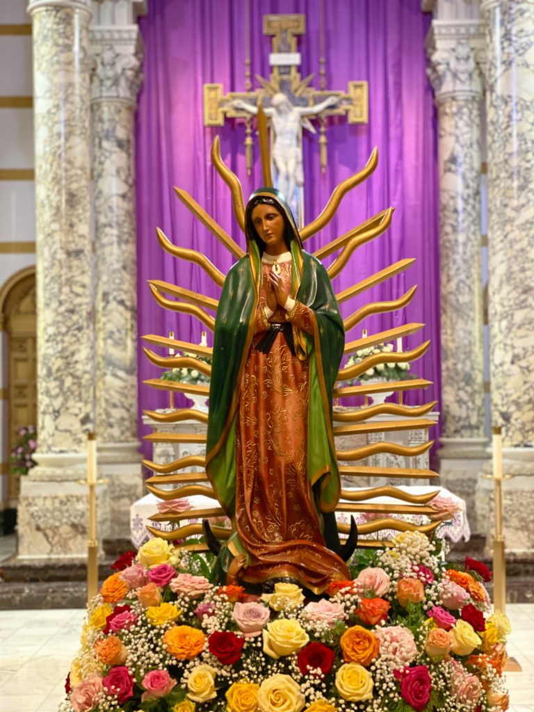 Elegant Virgin Mary statue adorned with vibrant flowers in a Catholic church.